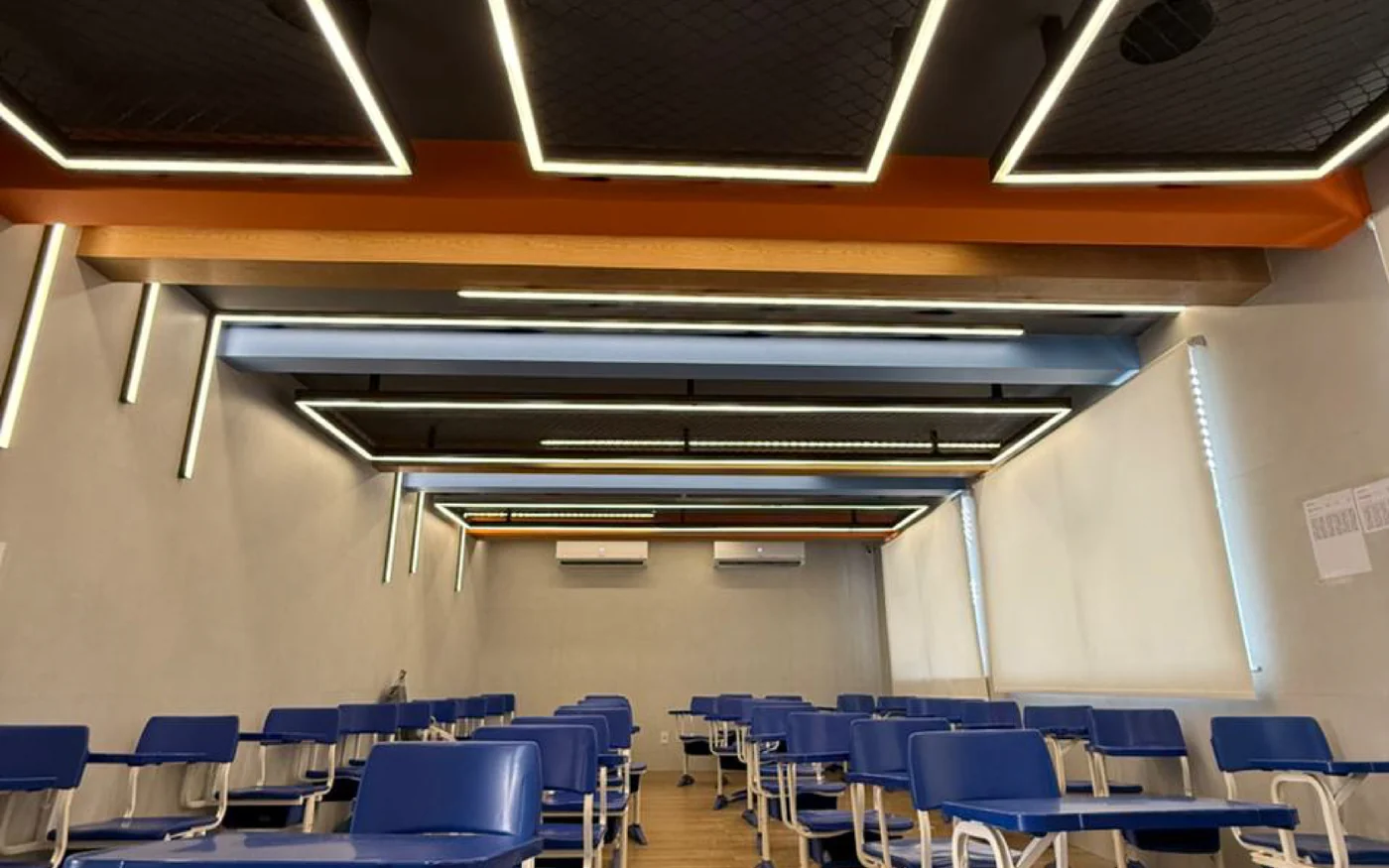 Sala de aula do Colégio Aprendiz com carteiras azuis e iluminação no teto